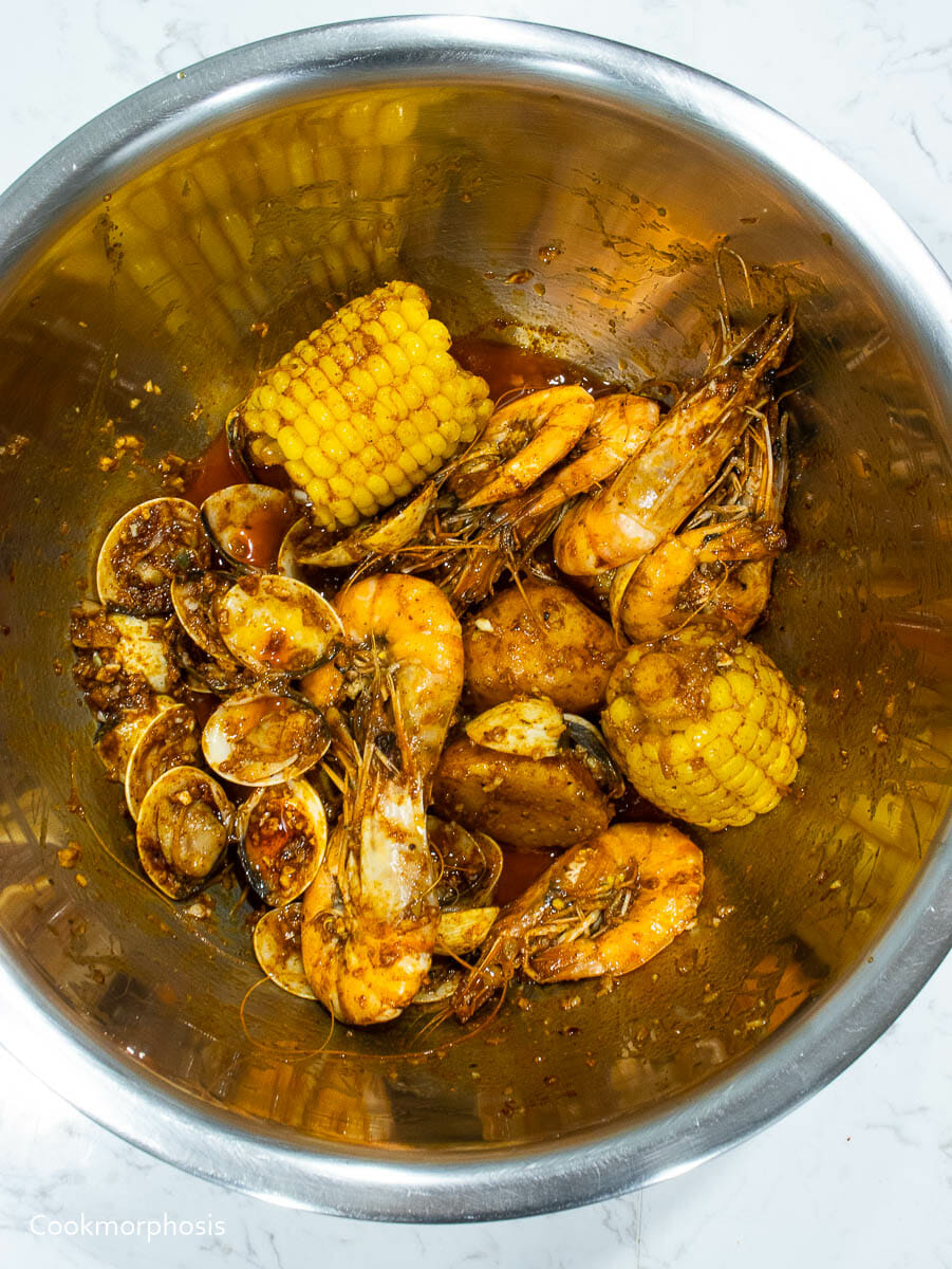 a bowl of garlic butter Cajun seafood boil including shrimps, clams, corns, and potatoes