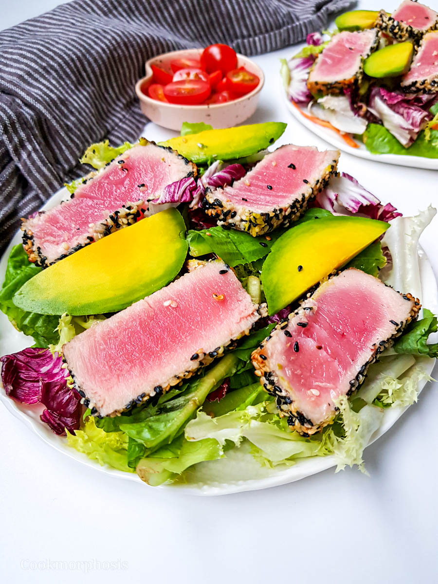 a plate of green salad that includes seared tuna coated with black and white sesame and fresh slices of avocados