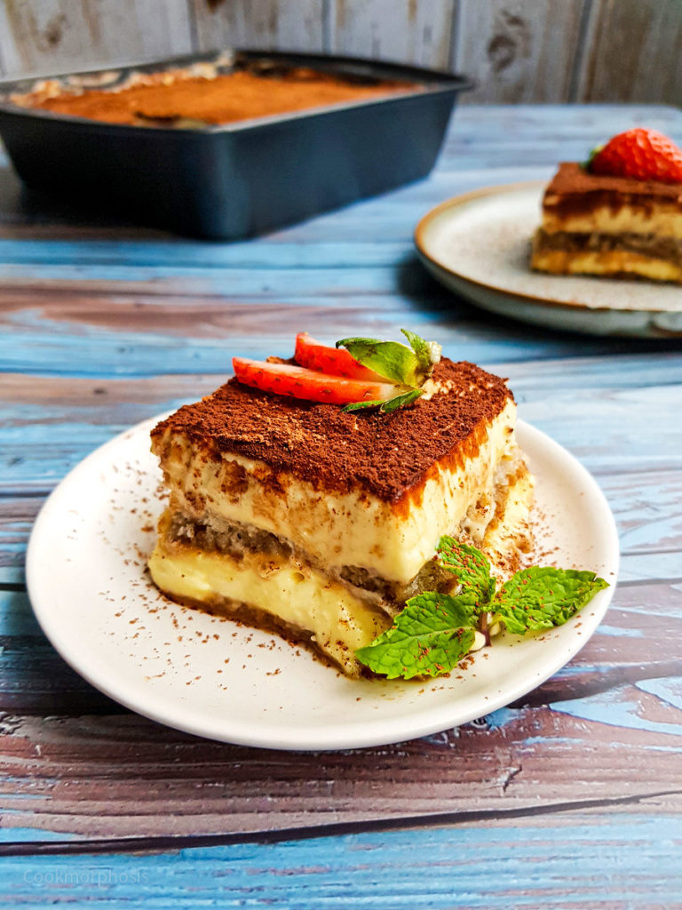 authentic tiramisu, a restaurant style dessert, is served with slices of fresh strawberries and mint leaves