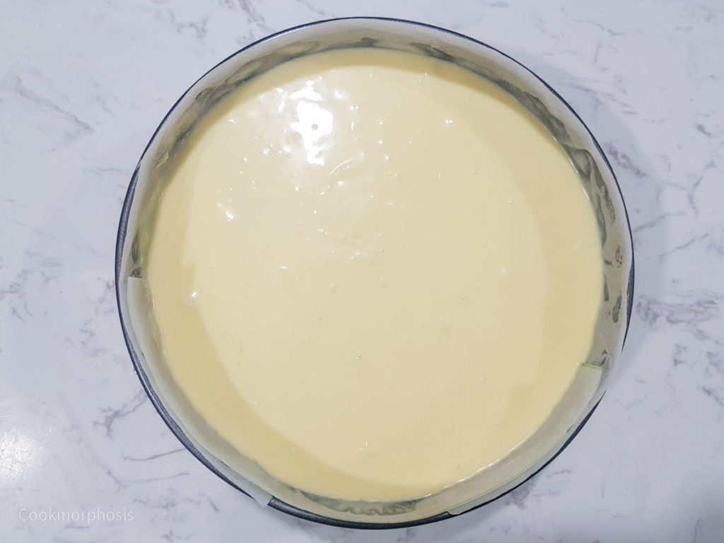 cheesecake batter is poured inside a springform pan that was lined with parchment paper inside