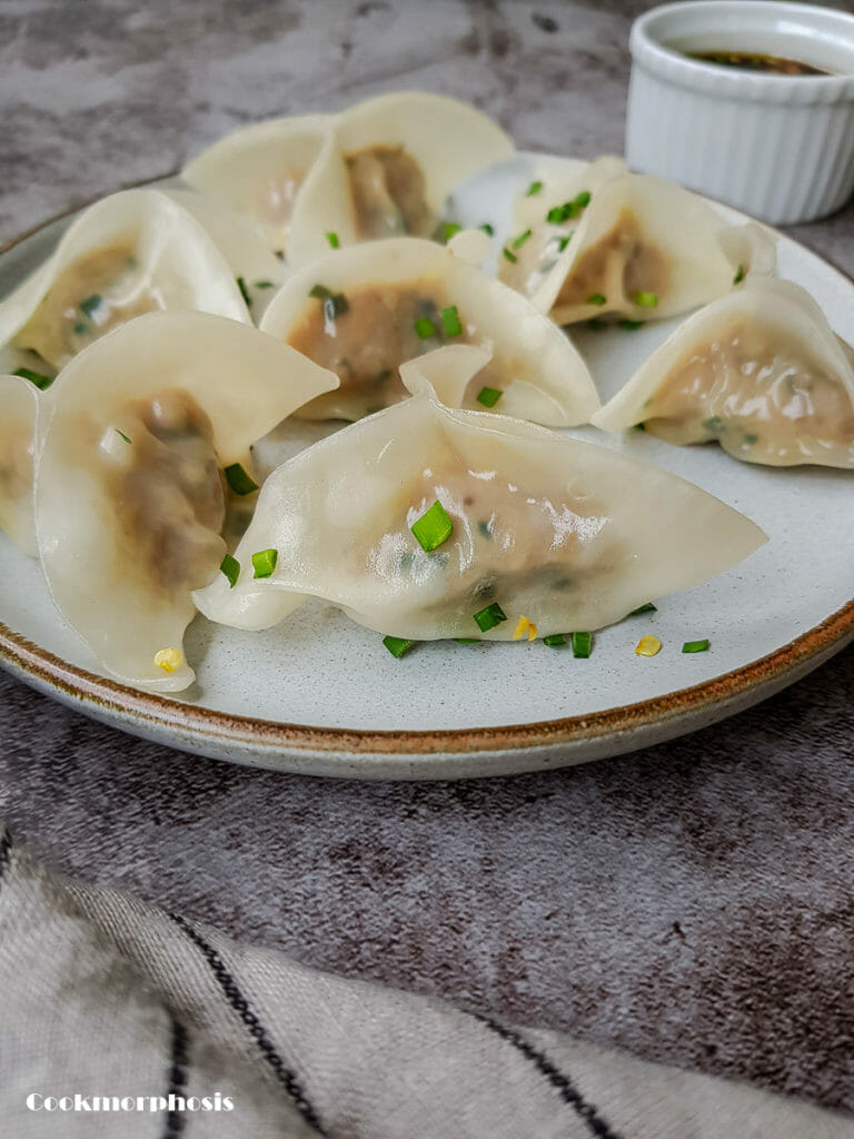7 pork and chive dumplings put on a white plate next to dumpling dipping sauce