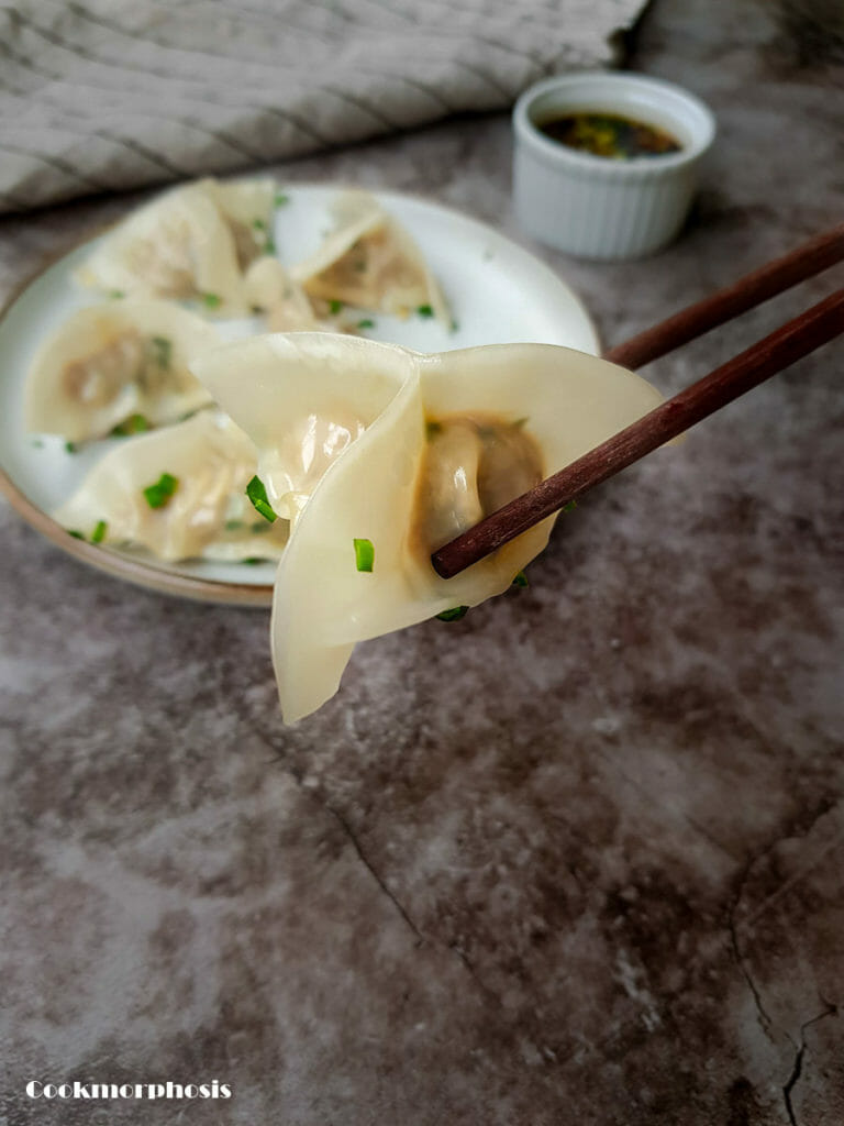 a nice dumpling is hold by a chopstick with dumpling dipping sauce is in the background