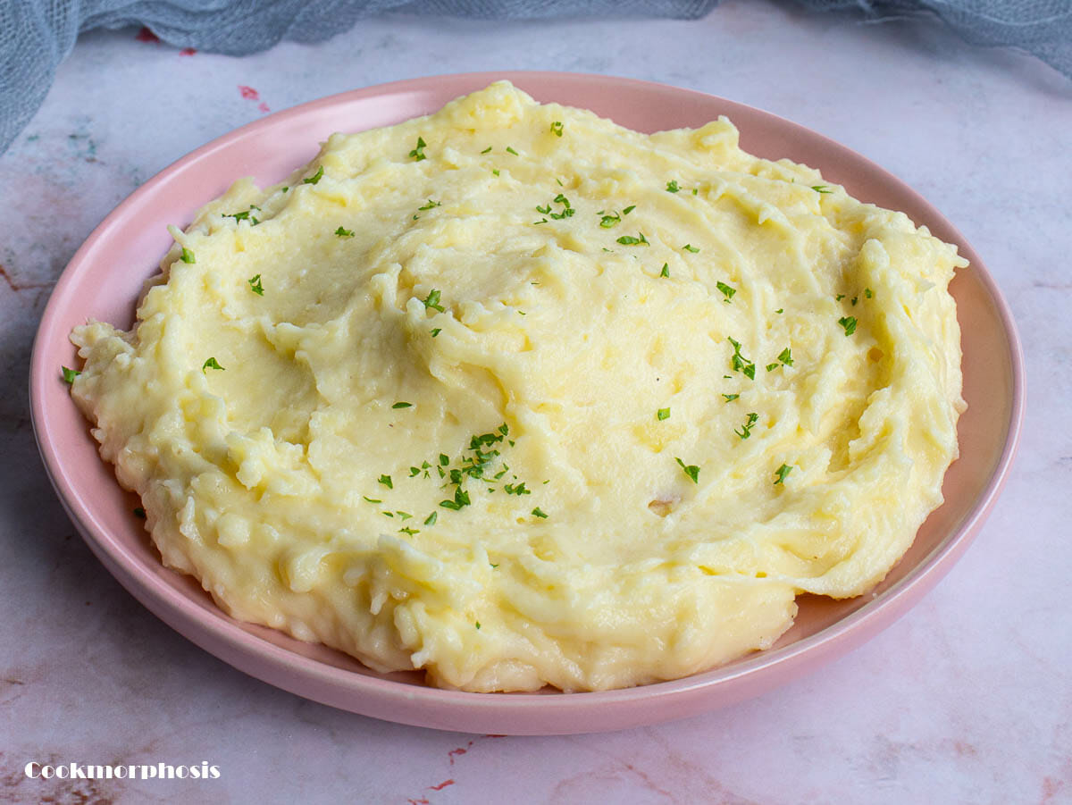 mashed potatoes are put on a pink plate and garnished with minced parsley