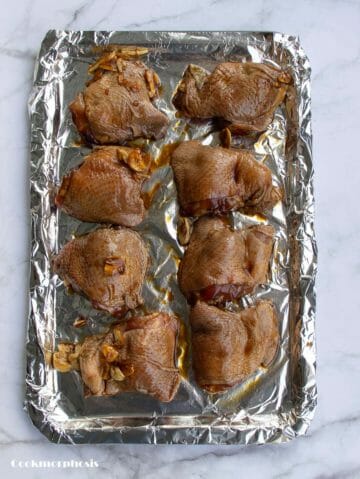 8 soy sauce chicken thighs are arranged nicely on a rimmed baking sheet lined with aluminum foil