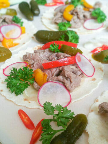 a close-up of no-grilled flank steak taco topped with bell pepper, parsley, slices of parsnip