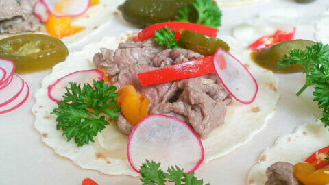 a close-up of no-grilled flank steak taco topped with bell pepper, parsley, slices of parsnip