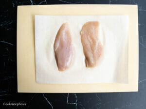 2 halves of chicken breasts putting on cutting board lined with parchment paper