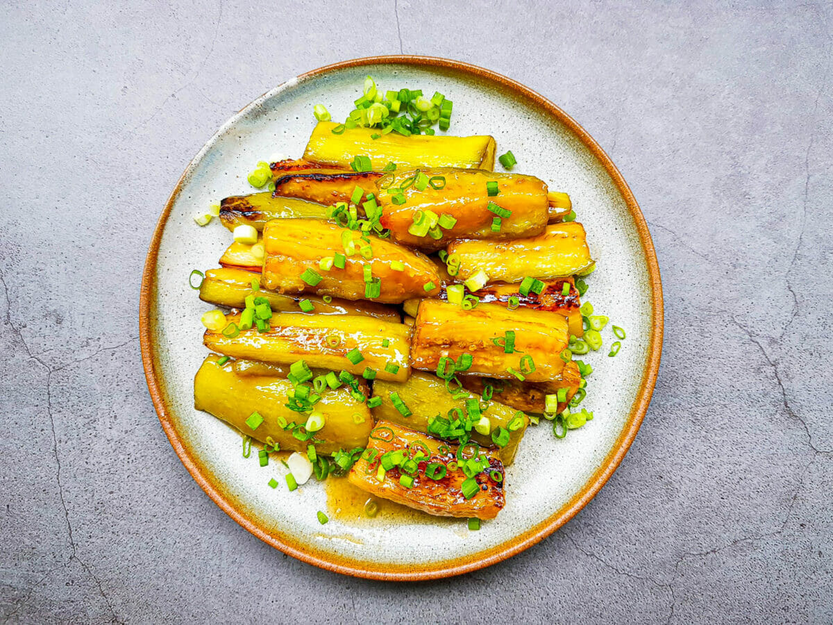 a plate of eggplant stir fried with white miso sauce and topped with green onion