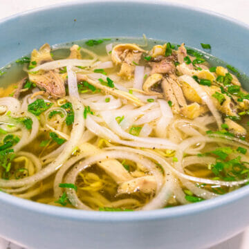 a huge bowl of authentic homemade chicken pho topped with sliced white onion, chopped cilantro and green onion