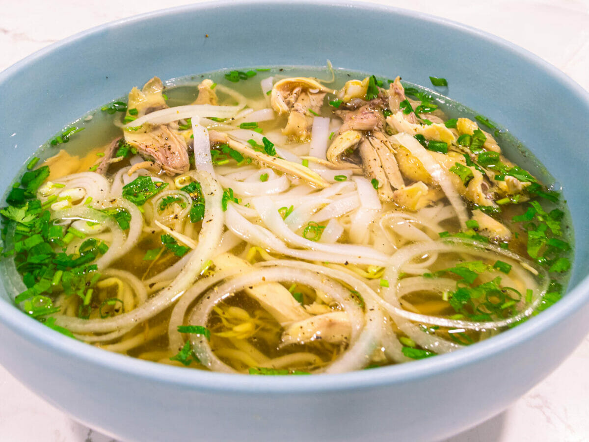 a huge bowl of authentic homemade chicken pho topped with sliced white onion, chopped cilantro and green onion