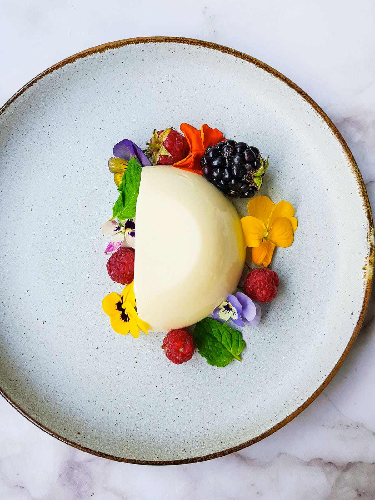 half of cream coconut panna cotta put on a plate and decorate with fresh fruit, edible flowers and mints