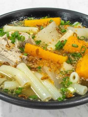 a bowl of macaroni soup with pork ribs, carrot, daikon, green onion and fried garlic
