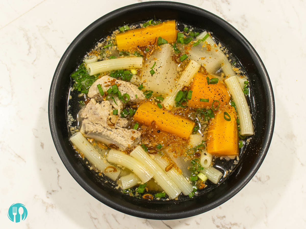 a bowl of macaroni soup with carrot, daikon and garnished with green onion