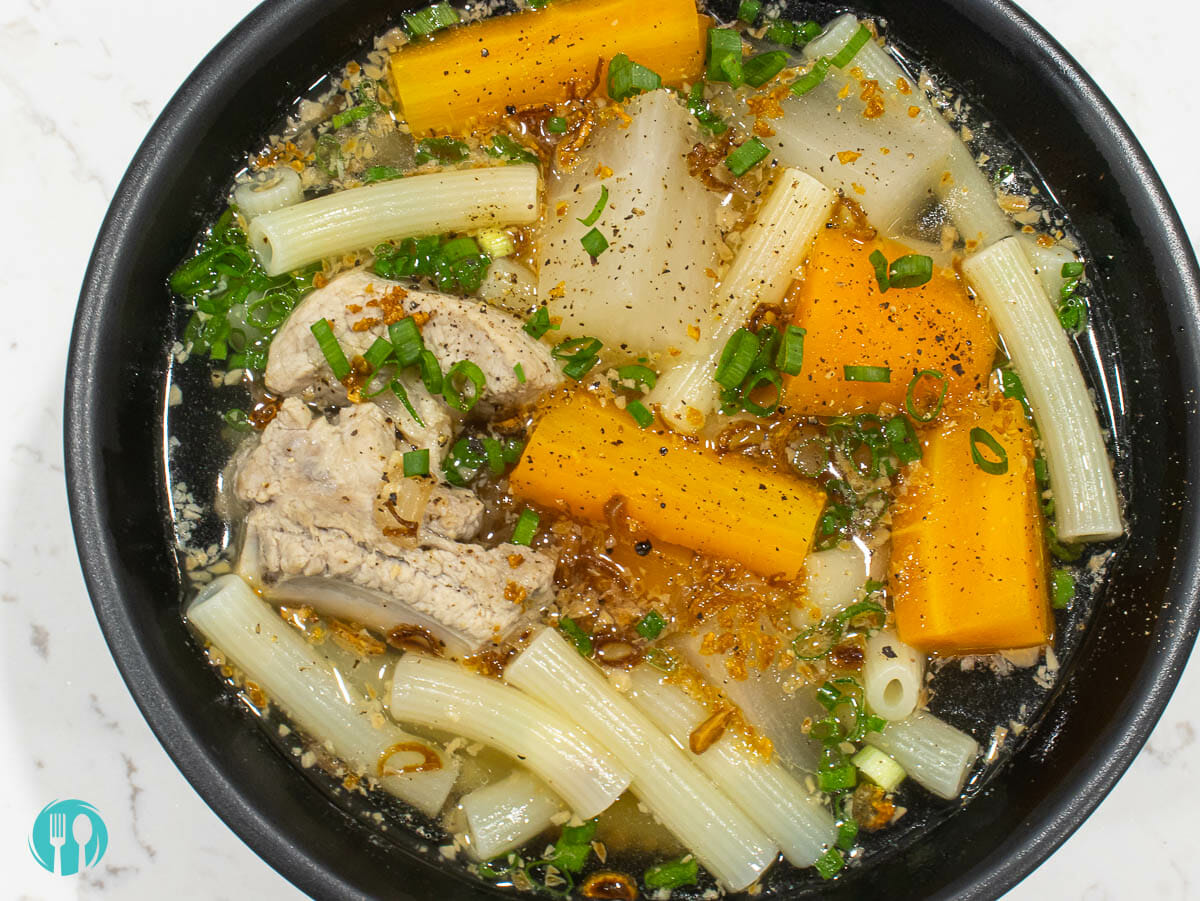 a bird eye view of a bowl of vietnamese pork ribs macaroni soup with carrot and daikon