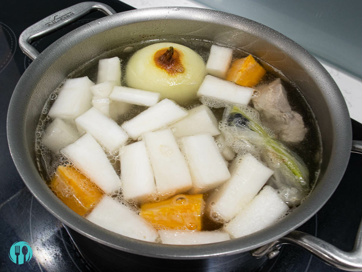 a hot boiling pot includes white onion, daikon, carrot, and pork ribs
