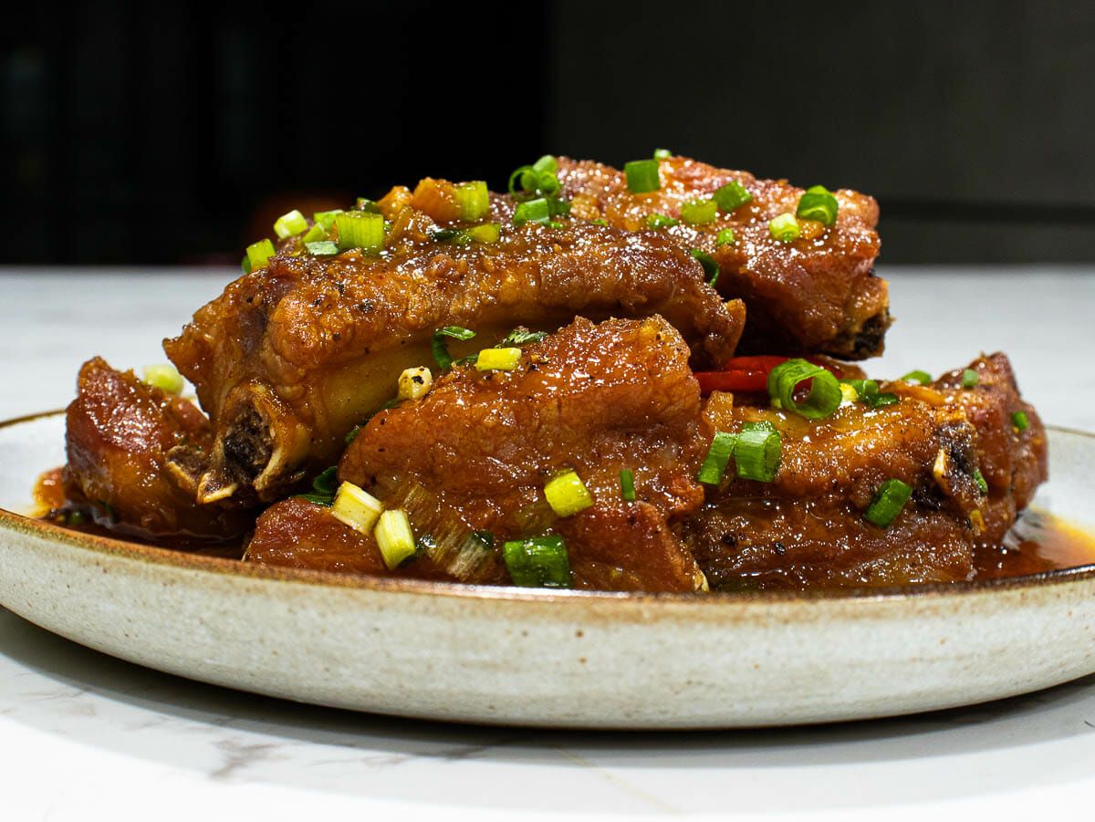 braised pork ribs garnished with green onion on a white plate