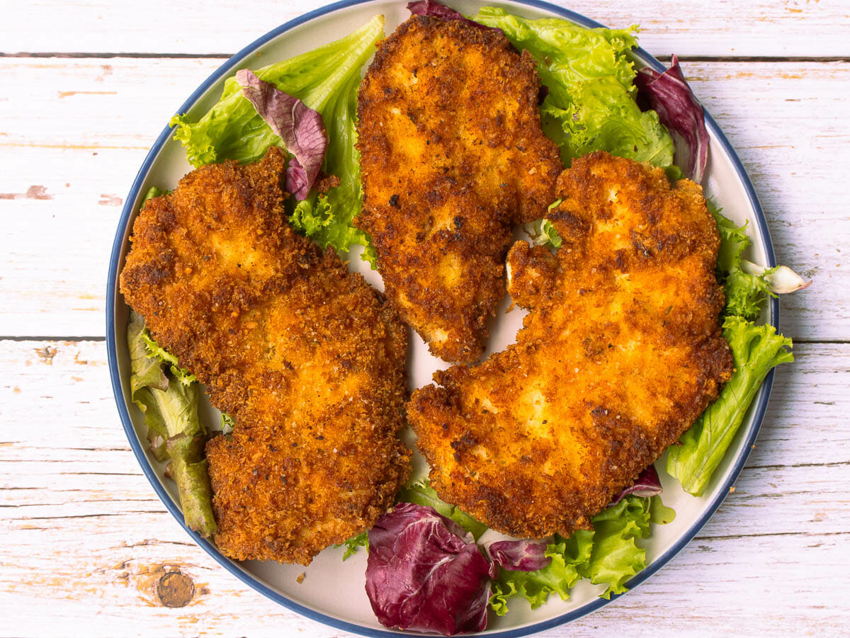 3 pieces of parmesan chicken cutlets put on a white round plate with lettuce