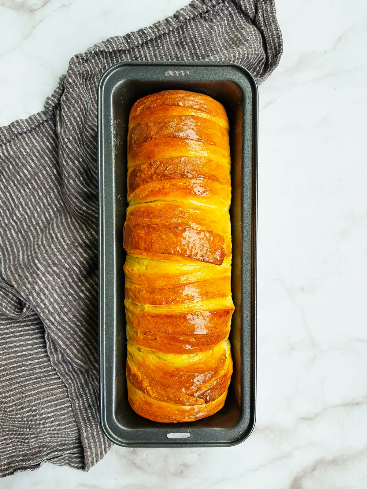 a loaf of fluffy condensed milk bread in a baking pan put next to grey kitchen towel