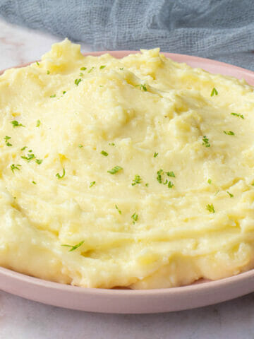 a plate of cheesy creamy mashed potatoes garnished with chopped parsley