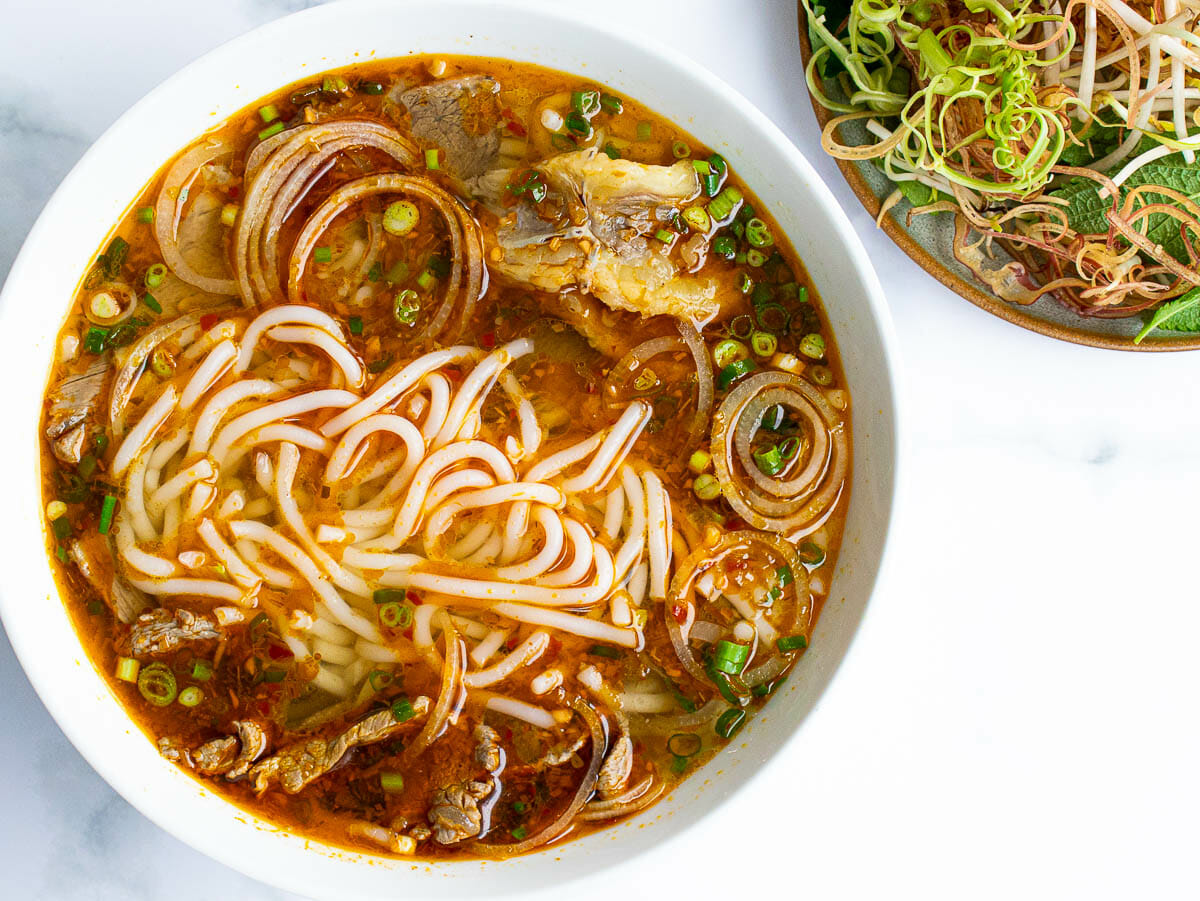 a bowl of bun bo hue and a plate of assorted herbs