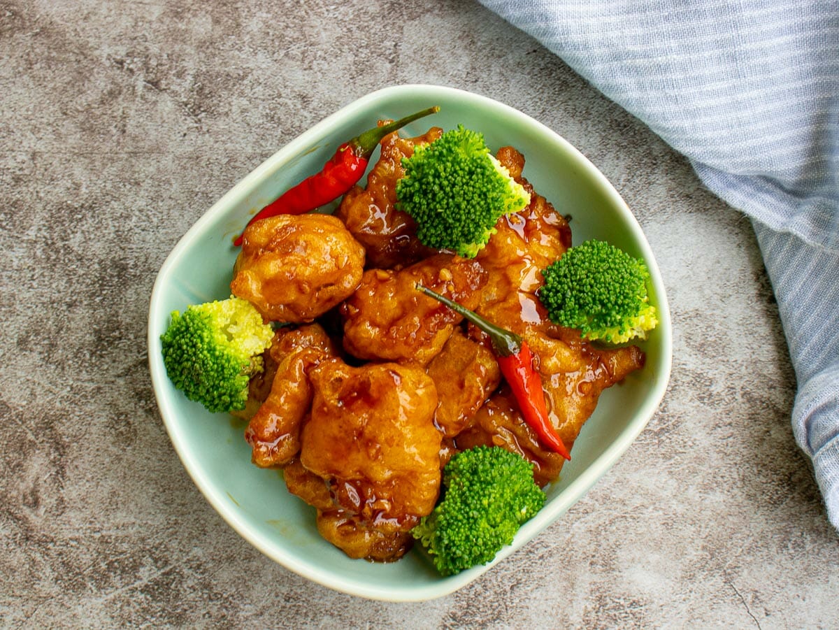 general tso's chicken with steamed broccoli and red chilies put in a green bowl