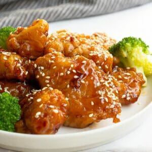 a plate of chinese sesame chicken with steamed broccoli as garnish