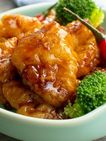 a bowl of general tso's chicken with steamed broccoli and red chilies
