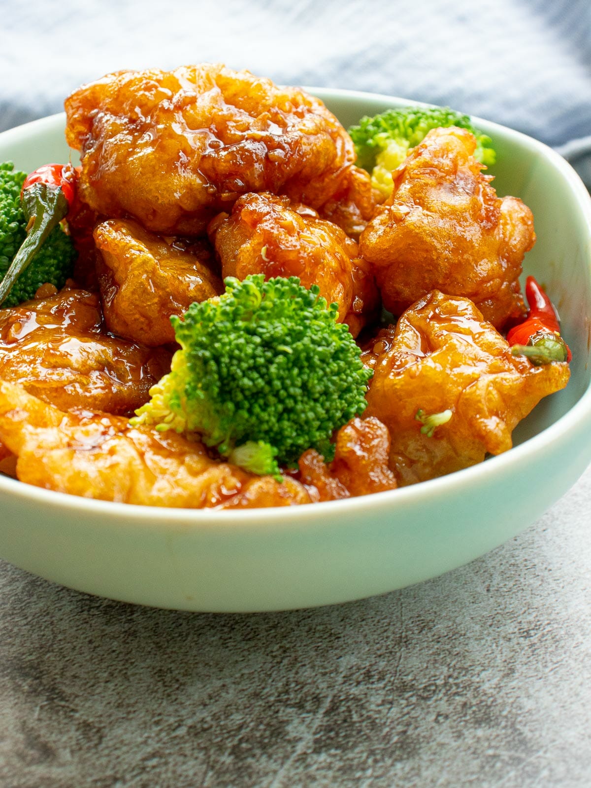 a whole bowl of crispy fried chicken coated in sticky sweet spicy sauce with 1 steamed broccoli