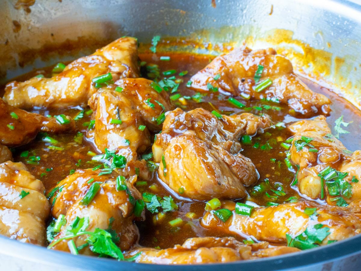 a pan of chicken cooked in sweet and spicy sauce and garnished with chopped cilantro and green onion