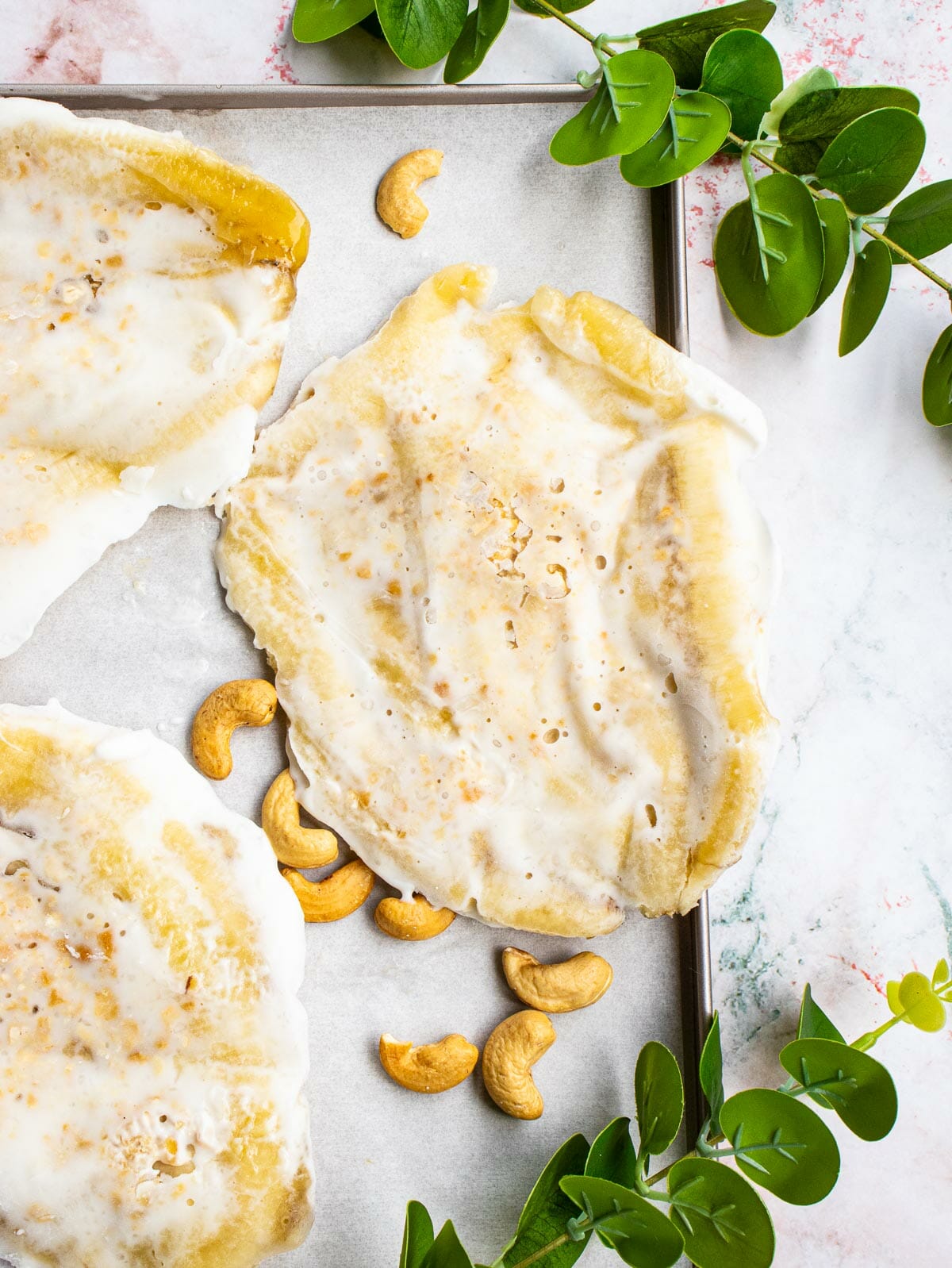 1 piece of vegan banana coconut ice cream put on a baking tray next to few roasted cashews