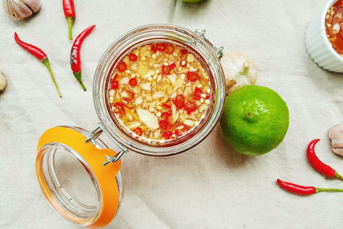a bird-eye view of a jar of nước mắm put next to a lime, few red chilies and cloves of garlic