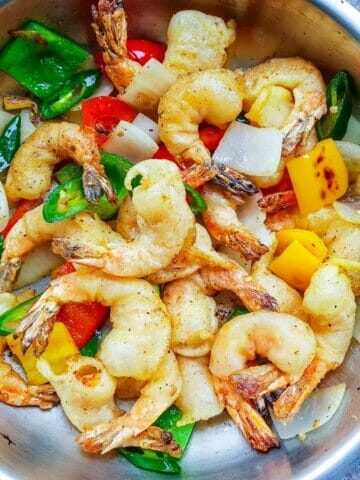 a pan of Chinese salt and pepper shrimps with green and red belly pepper, white onion, and slices of jalapeno