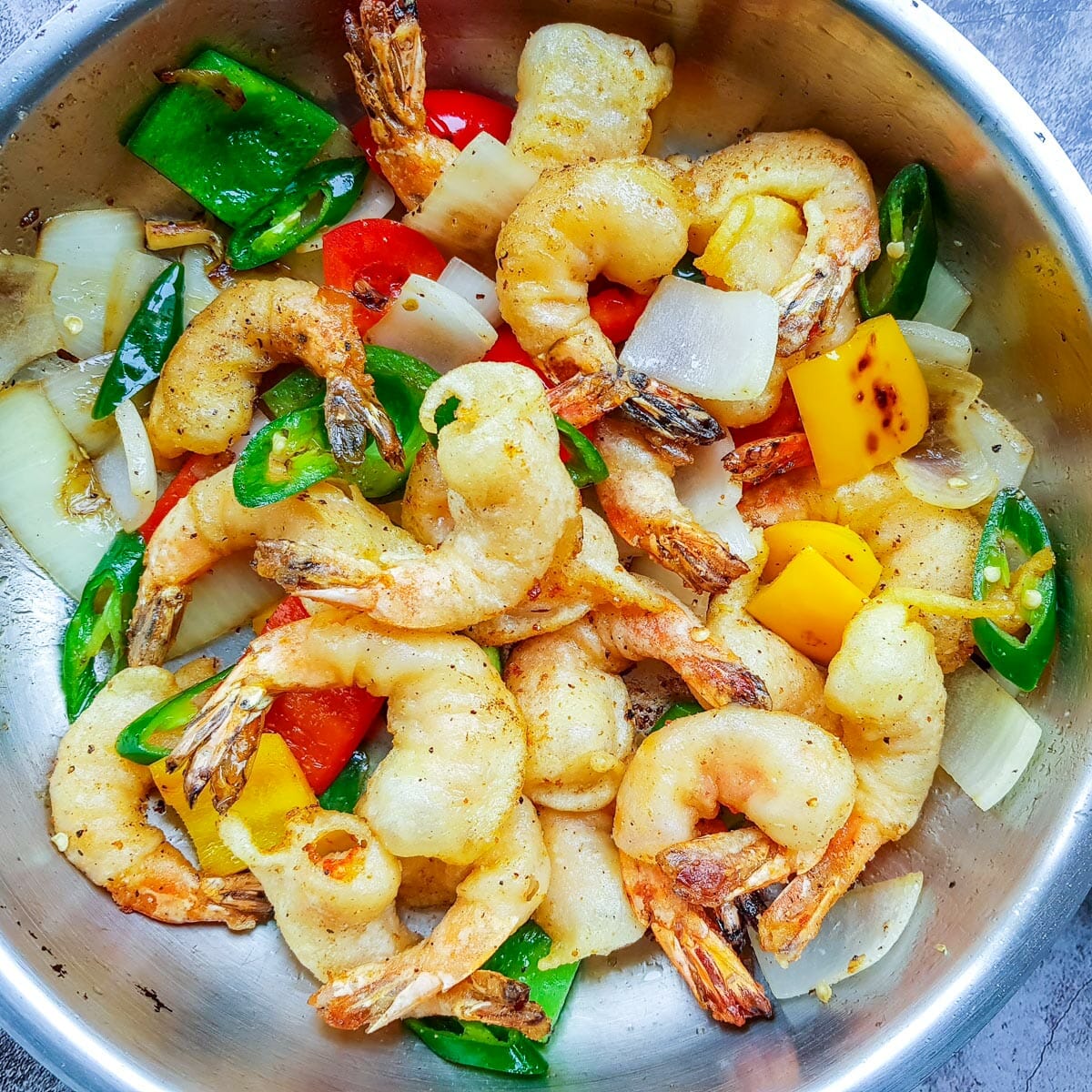 a pan of Chinese salt and pepper shrimps with green and red belly pepper, white onion, and slices of jalapeno