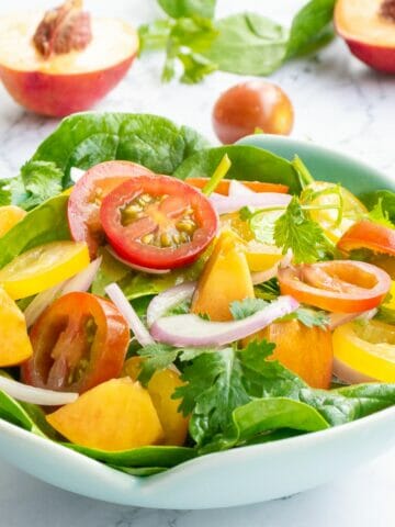 a bowl of tomato peach salad mixed with spinach and cilantro leaves