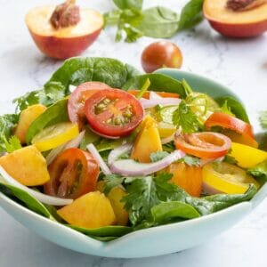a bowl of tomato, peach, spinach, cilantro, red onion salad