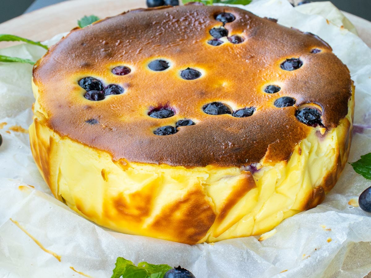 a side view of a whole cheesecake made with blueberries and put on a parchment paper