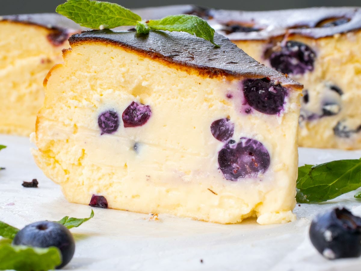 a side view of a cheesecake slice garnished with mint leaves and fresh blueberries