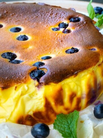 a angle view of a whole blueberry basque burnt cheesecake with a few of mint leaves as garnish