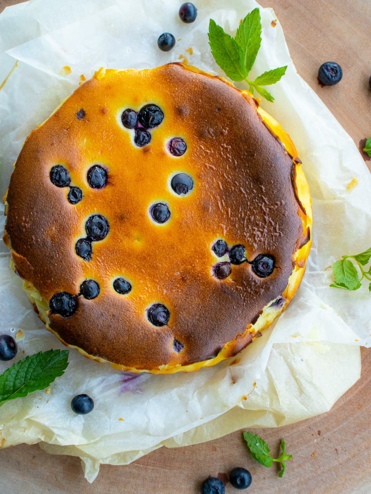a bird eye view of a whole blueberry cheesecake put on a parchment paper and garnished with mint leaves
