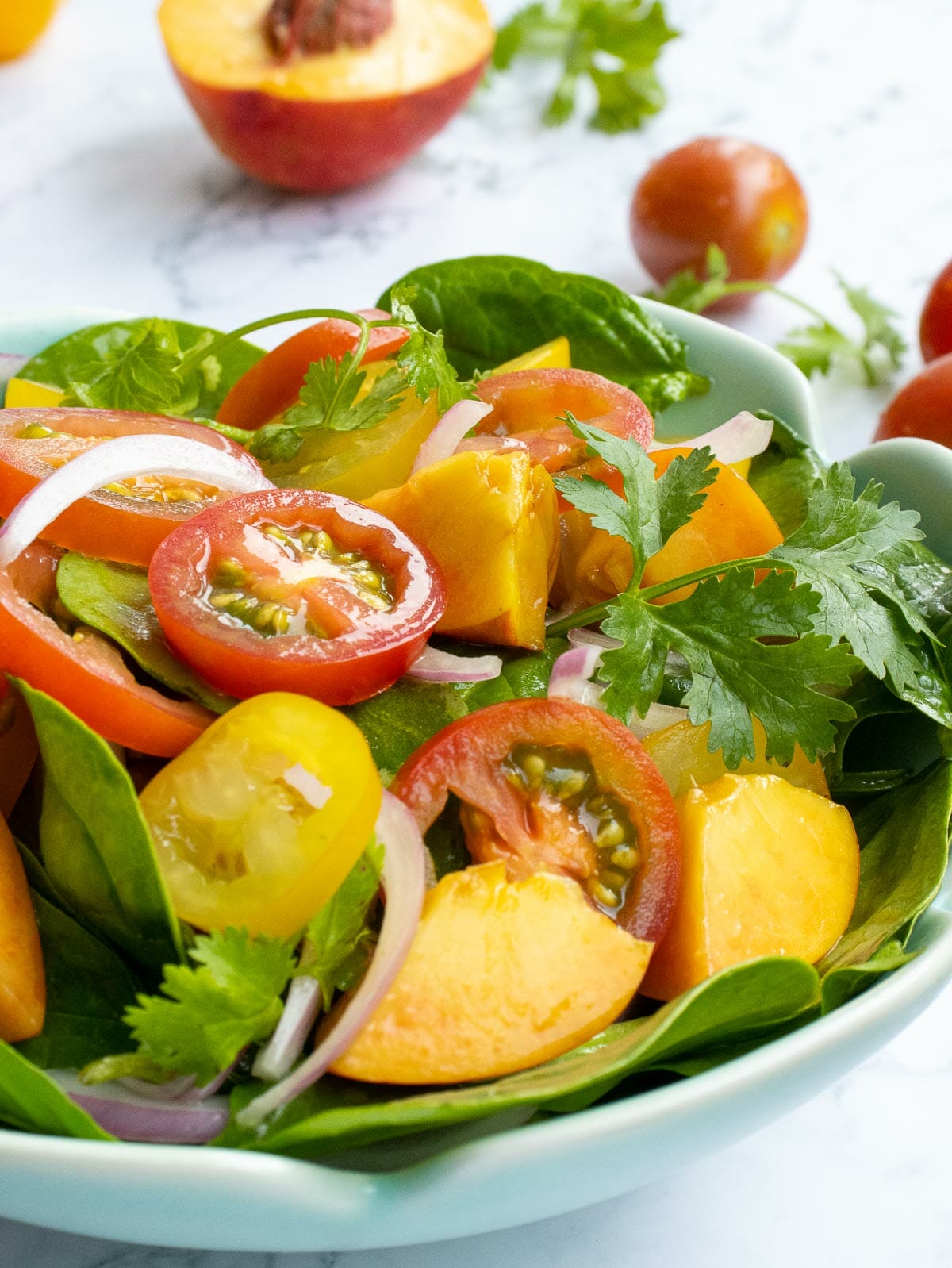 a close up of a bowl of spinach salad with freshly cut tomatoes, peaches, and cilantro