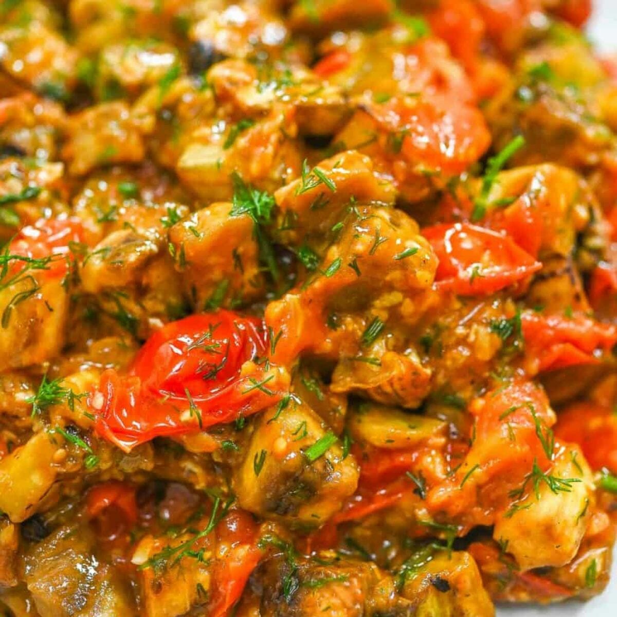 a plate of stir-fried eggplant in tomato sauce and topped with chopped dill