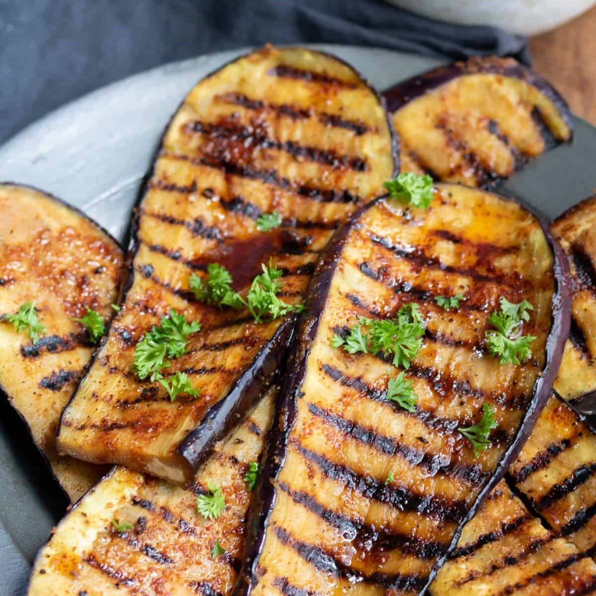 a plate of smokey grilled eggplant steaks with grill marks and topped with chopped parsley