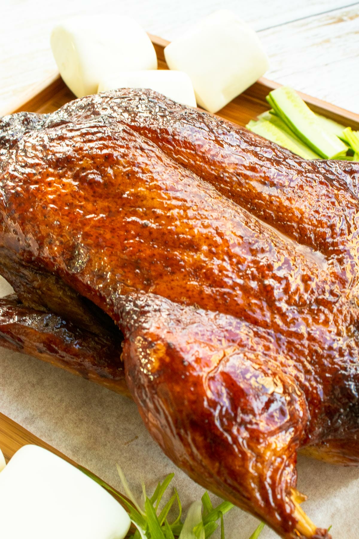 a close up of a juicy whole roast duck put next to mantou and slices of cucumber