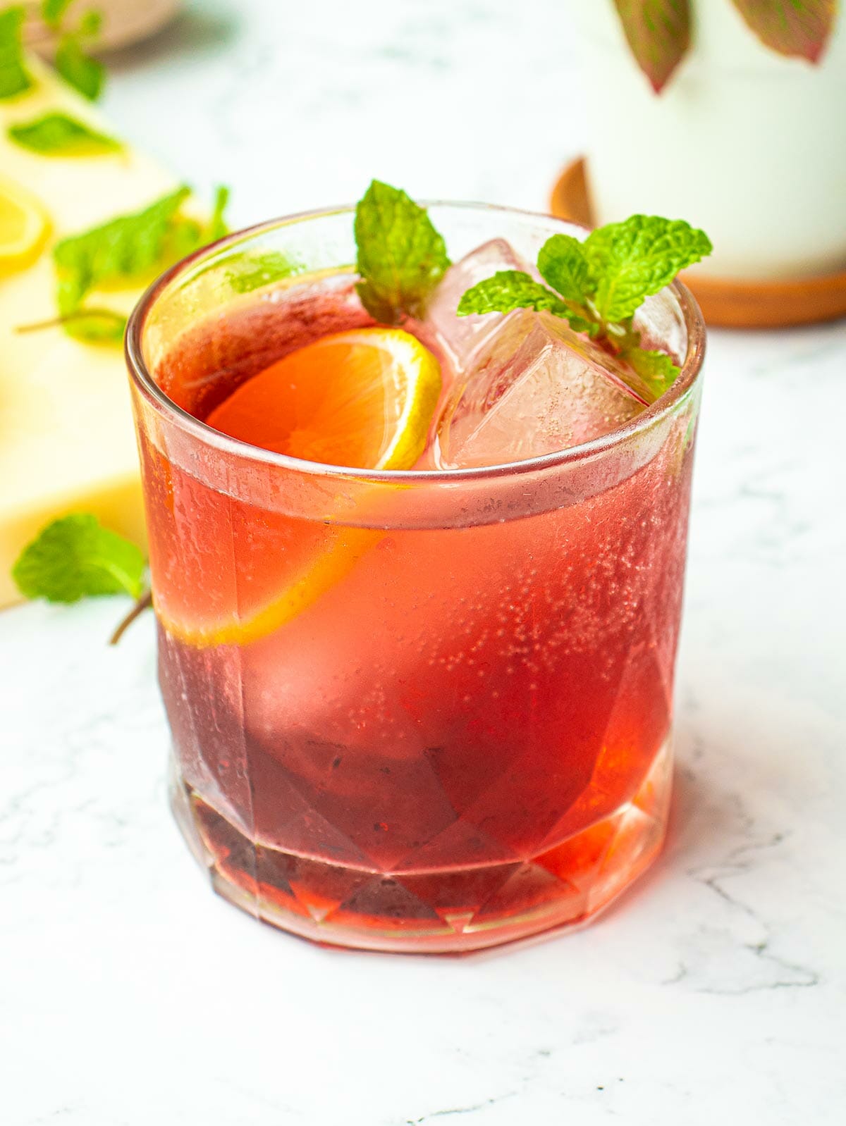 a glass of cranberry juice on ice and garnished with mint leaves and a slice of lemon