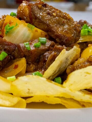 a plate of sauteed beef with potato chips garnished with chopped green onion