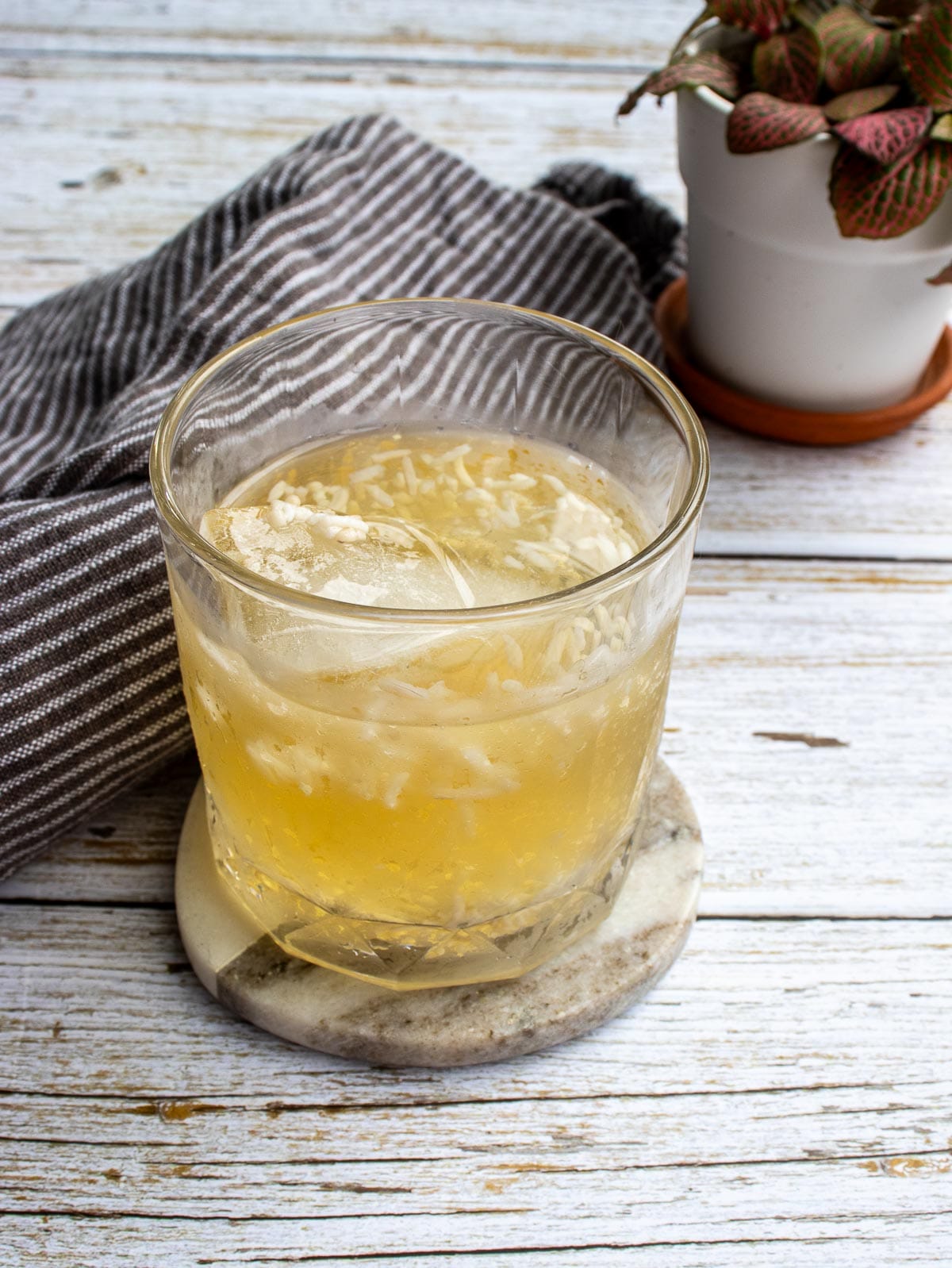 A cup of Korean sikhye drink on ice put next to a grey kitchen towel