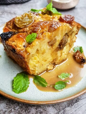 a big slice of brioche raisin bread pudding garnished with mint leaves and sweet coffee sauce