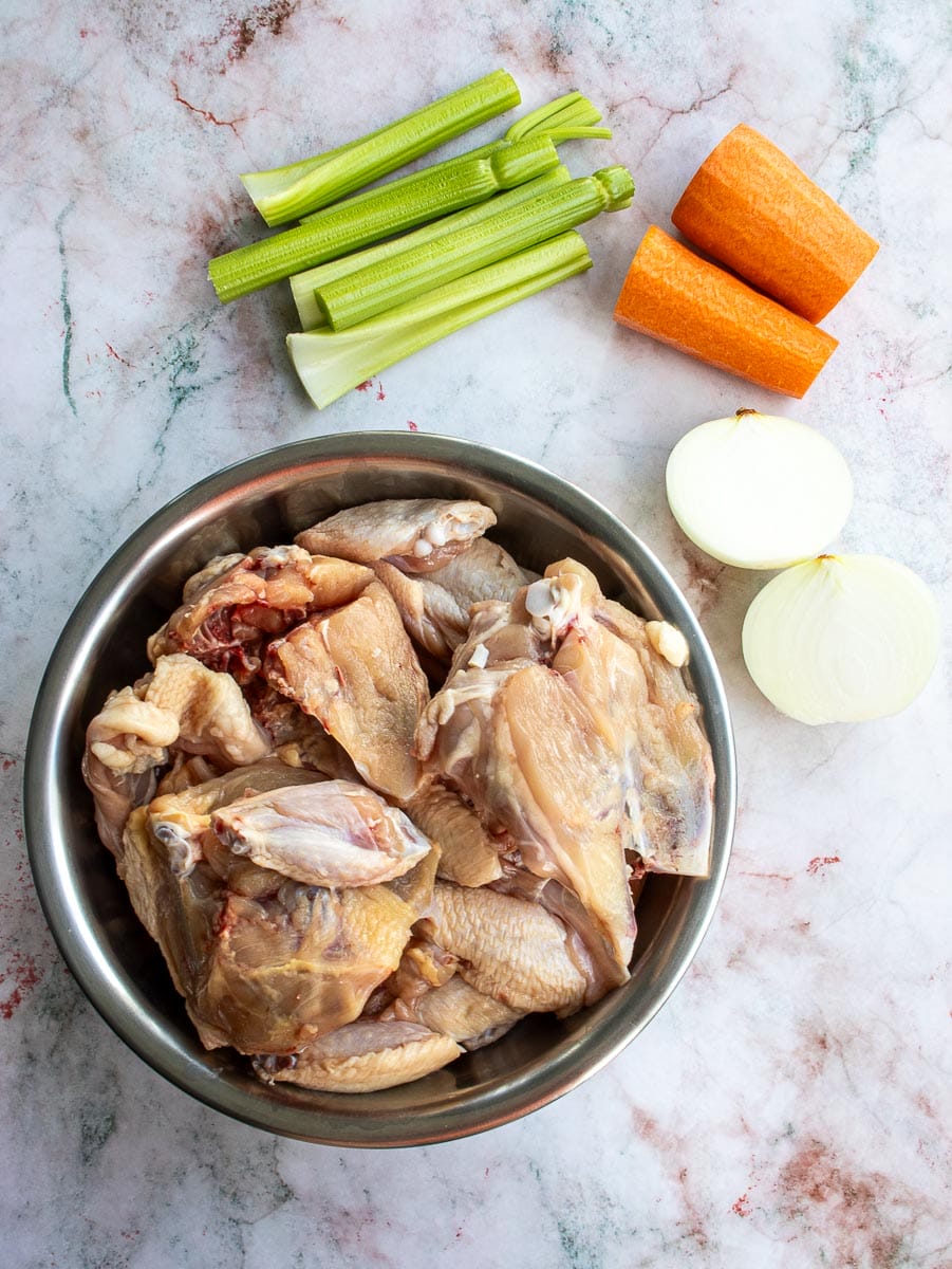 Ingredients to make the best chicken bone broth: whole carcass of chicken, celery, carrot, and white onion