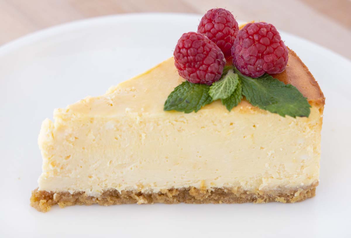 a slice of chicago style cheesecake topped with fresh raspberry and mint leaves