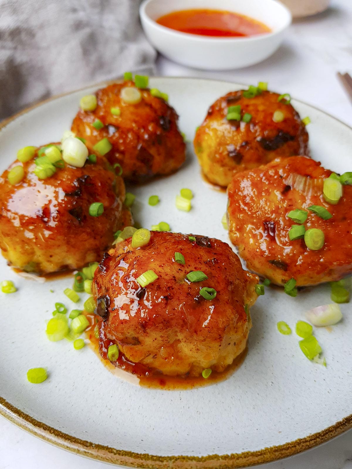 a close up of 5 sweet ground turkey meatballs garnished with chopped green onion and served with Thai sweet chili sauce on the side